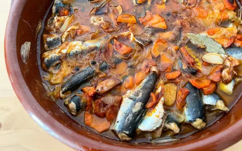 Sardinas en escabeche cocinándose en una cazuela de barro con verduras.
