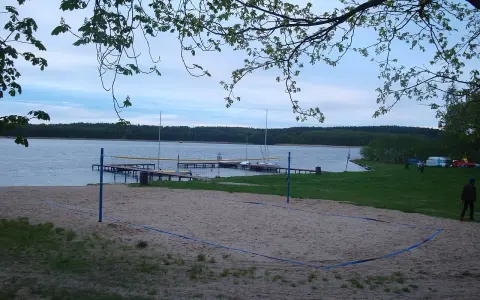 Plaża z boiskiem do siatkówki plażowej nad jeziorem w Borneńskim Sulimowie. W tle pomosty, żaglówki i las.
