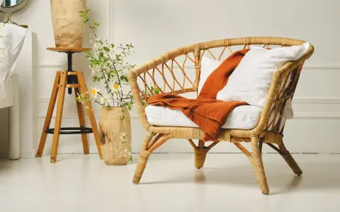 Un fauteuil en rotin tressé, invitant à la détente. Un plaid orange et un coussin blanc ajoutent une touche de confort. L'entretien rotin est essentiel pour préserver sa beauté naturelle.