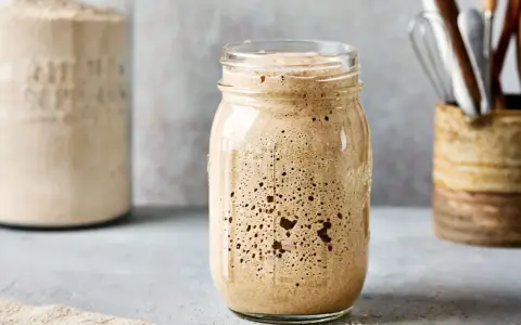 Aktiver Sauerteig im Glas, bereit für das Ansetzen mit dem Thermomix. Daneben ein Glas mit Mehl und ein Behälter mit Küchenutensilien.