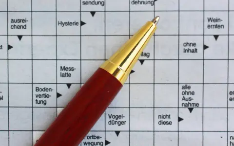 Ein roter Stift liegt auf einem Kreuzworträtsel mit deutschen Begriffen.