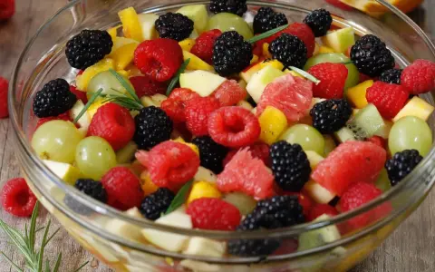 Un bol de salade de fruits frais et colorée, garnie de framboises, mûres, raisins verts, morceaux de pomme, pamplemousse et kiwi.