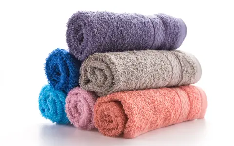 Pile de serviettes de bain roulées aux couleurs vives : violet, bleu, gris, rose et corail. La matière douce invite à la détente.