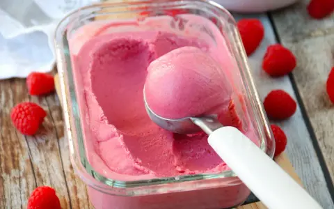 Glace framboise sans sorbetière, on dirait qu'elle est faite avec du lait concentré. Une boule est prélevée avec une cuillère.
