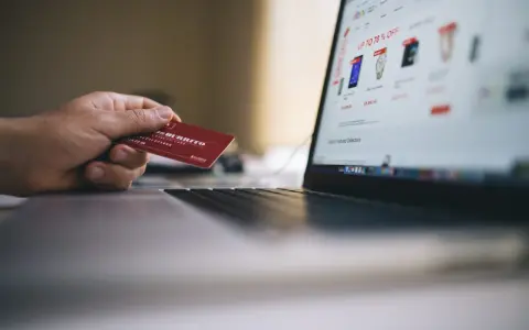 Dłoń trzyma kartę lojalnościową, przygotowując się do zakupów online. Może to być import z Wielkiej Brytanii, np. z sieci sklepów.