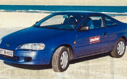 Niebieski Toyota Paseo stoi na plaży, z morzem w tle.