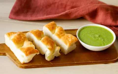 Focaccia tagliata a pezzi su tagliere di legno, accanto a una ciotola di pesto di salvia.