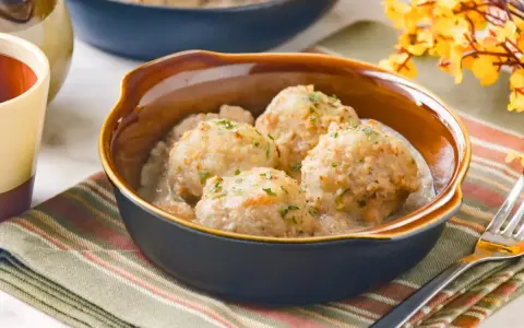 Cuatro albóndigas de merluza caseras en una cremosa salsa, espolvoreadas con perejil fresco.