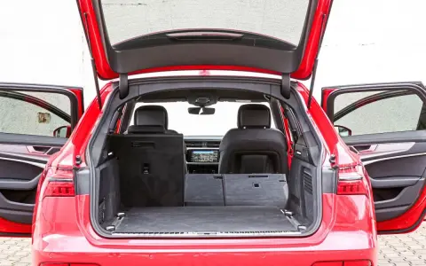 Czerwone Audi A6 Avant z otwartą klapą bagażnika i drzwiami. Wnętrze pokazuje przestronny bagażnik, idealny na wakacyjne wyjazdy, z możliwością powiększenia przestrzeni po złożeniu siedzeń.