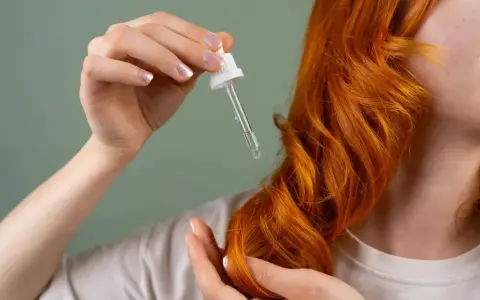 Dłoń z pipetką aplikuje olejek na rude włosy. Zastanawiasz się, ile trzymać olej na włosach?