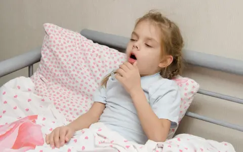 Mała dziewczynka z **przewlekłym kaszlem u dziecka** leży w łóżku, trzymając termometr.
