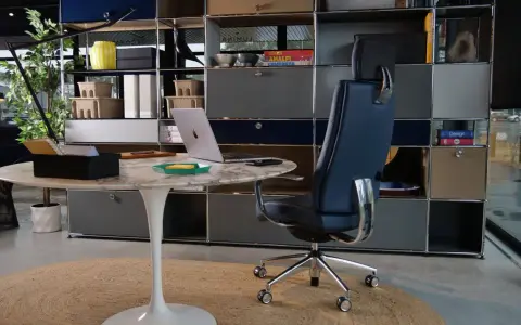 Un fauteuil de bureau design bleu marine, un bureau rond en marbre et un ordinateur portable créent un espace de travail élégant.