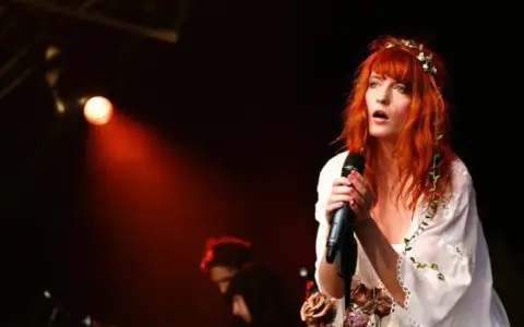 Florence Welch, una de los miembros de Florence and the Machine, canta con pasión en el escenario, iluminada por una luz roja.