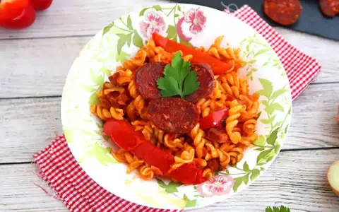Pyszny makaron z chorizo, papryką i natką pietruszki na talerzu z motywem kwiatowym.