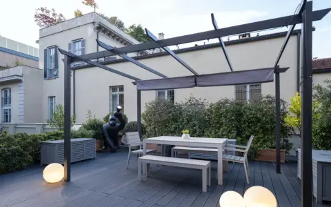 Terrazze arredate con tavolo, panche, sedie e scultura di gorilla sotto una pergola. Illuminazione soffusa con sfere luminose.