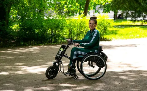 Kobieta w wózku inwalidzkim z napędem elektrycznym, który mógł zostać sfinansowany dzięki dofinansowaniu do wózka inwalidzkiego, cieszy się spacerem w parku.