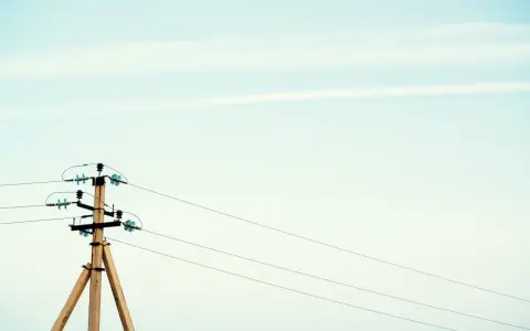 Drewniany słup na działce, który stoi tam od ponad 30 lat, z przewodami elektrycznymi na tle jasnego nieba.