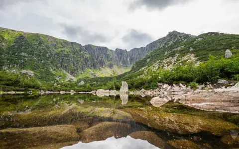 Spokojne, śnieżne stawy odbijają skaliste szczyty i zielone zbocza gór.