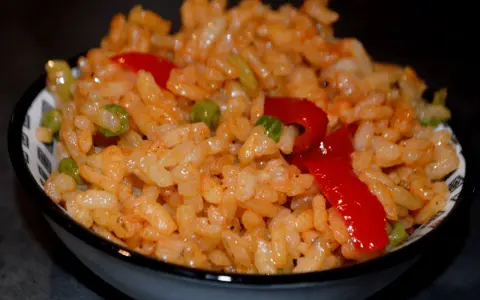 Un bol de riz coloré avec des petits pois et des poivrons rouges, parfait pour une recette salade riz facile et rapide.