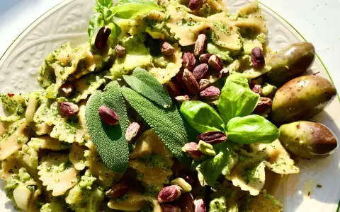 Farfalle condite con un saporito pesto di salvia, guarnite con pistacchi, basilico e olive.