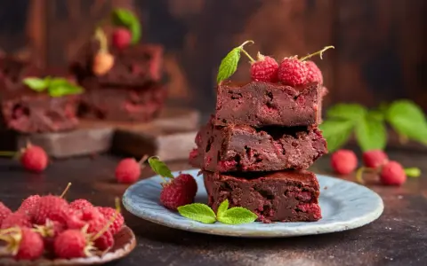 Stos pysznych brownie z malinami, ozdobiony świeżymi malinami i listkami mięty.