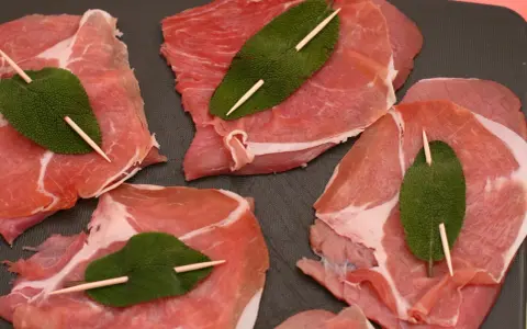 Fette di vitello pronte per la saltimbocca alla romana ricetta originale, con prosciutto crudo e foglie di salvia fissate con stuzzicadenti.