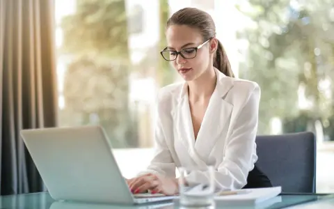Kobieta w okularach pracuje przy laptopie, zastanawiając się, ile zarabia pracownik banku.