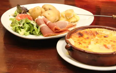 Un plat de spécialité auvergnate : pommes de terre, jambon cru, salade et un gratin de fromage fondant.