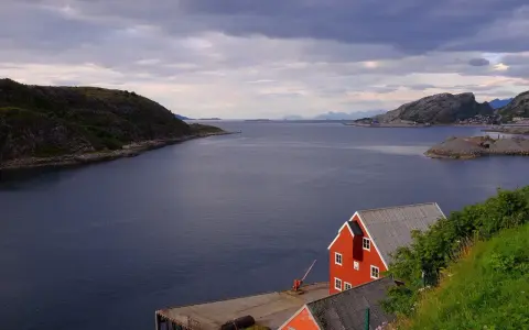 Widok na fiord, czerwone domy rybackie i góry w tle. Prom Bodo Moskenes czeka na podróżnych.