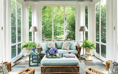 A serene screen porch with rattan furniture, plush cushions, and lush greenery. The natural screen porch materials create a cozy, inviting atmosphere.