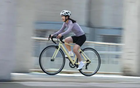Uśmiechnięta kobieta w kasku pędzi na rowerze, ciesząc się sportami rowerowymi.