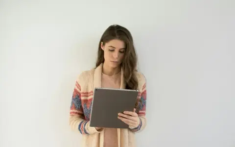 Kobieta w swetrze z wzorem przegląda tablet, być może szukając informacji o długoterminowym zwolnieniu lekarskim.