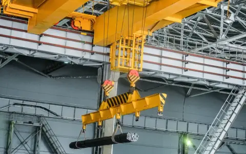 Udt suwnice pytania i odpowiedzi: żółta suwnica podnosi wiązkę prętów w hali produkcyjnej.