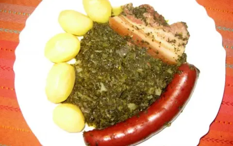 Gedünsteter Grünkohl mit Salzkartoffeln, Kassler und einer herzhaften Lungenwurst, die zum Kochen oder Braten bereit ist.