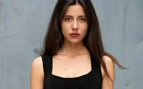 Ritratto di una giovane donna con lunghi capelli castani, indossa un abito nero. Il suo sguardo è intenso, come se stesse aspettando qualcuno, forse celeste dalla porta.