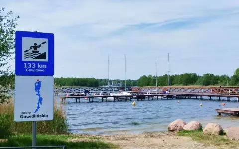 Znaki informują o 133 km do Gowidlina i o jeziorze Gowidlińskim. Widok na pomost z żaglówkami i kajakiem.