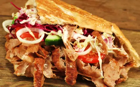 Kebab z mięsem, warzywami i sosem w bułce na drewnianym tle.