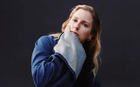 Susanne Sundfør w dżinsowej kurtce, z dłonią na policzku, jakby inspirowana utworem "Blómi".