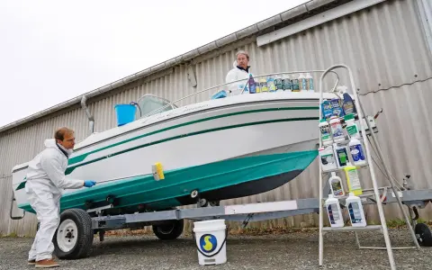 Un homme en combinaison blanche nettoie le flanc d'un bateau blanc et vert sur une remorque. Le nettoyage du pont du bateau est en cours.