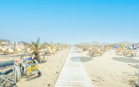 Una passerella bianca conduce alle spiagge di Riccione, con sdraio e ombrelloni pronti per accogliere tutti, compresa una sedia a rotelle speciale per la sabbia.