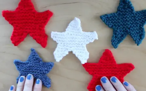 Cinco estrellas tejidas de punto estrella, rojas, blancas y azules, dispuestas sobre una superficie de madera.