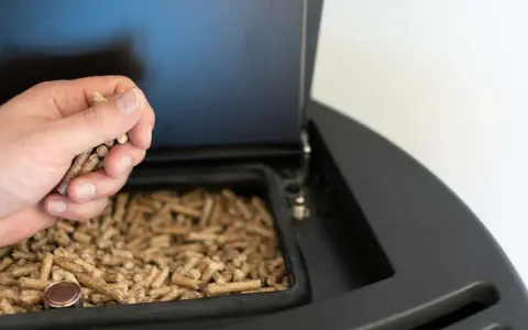 Mano cargando pellets en una estufa de pellets. Preparando la instalación de la estufa de pellets para un invierno cálido.