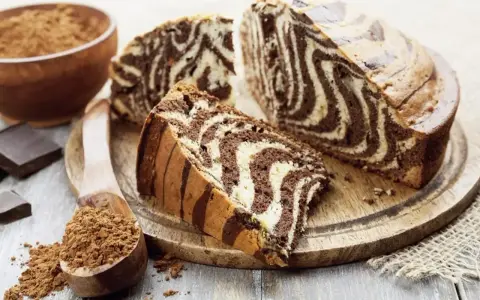 Wilgotne ciasto zebra z czekoladowymi i waniliowymi pasami, pokrojone na plastry, obok kakao i czekolady.