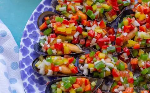Mejillones a la vinagreta, cubiertos con una colorida mezcla de pimientos picados y cebolla.