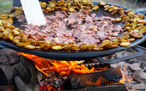 En stor stekpanna över öppen eld där kött och potatis tillagas. En perfekt dag att laga mat ute!