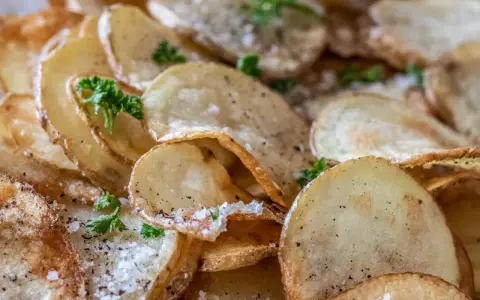 Krispiga, gyllene skivor av friterad potatis, strödda med salt och peppar, toppade med färsk persilja.