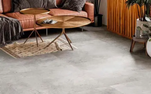 Un elegante soggiorno con divano in pelle color caramello, tavolini dorati e un tappeto etnico su un **pavimento grigio** che crea **abbinamenti** moderni e sofisticati.