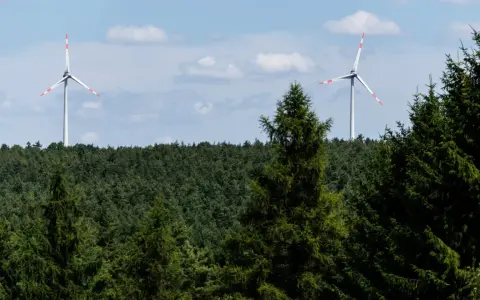 Zwei Windräder ragen über einen dichten Wald. Ein Onshore-Windpark in Deutschland, der saubere Energie erzeugt.