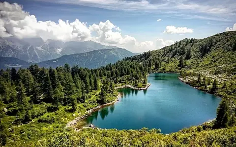Laghi di San Giuliano: un'oasi alpina con acque turchesi, circondata da fitti boschi di conifere e montagne maestose sotto un cielo azzurro con nuvole bianche.