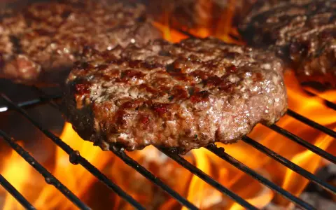 Soczyste kotlety wołowe smażące się na grillu z płomieniami.